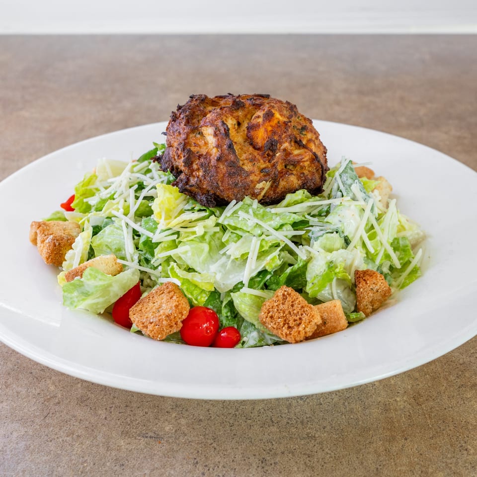Caesar salad topped with a crabcake.