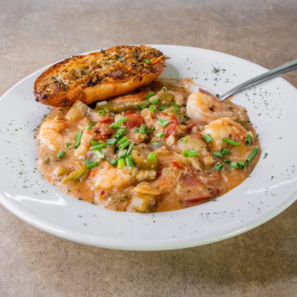 Creamy shrimp and vegetable dish garnished with green onions, served with toasted garlic bread on a white plate.
